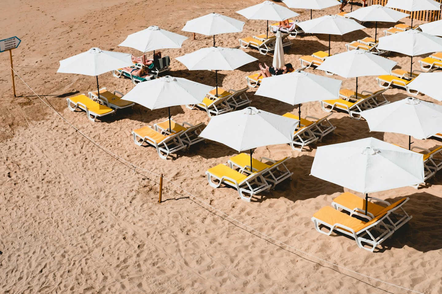 Persone rilassate su lettini gialli sotto ombrelloni bianchi su una spiaggia soleggiata.